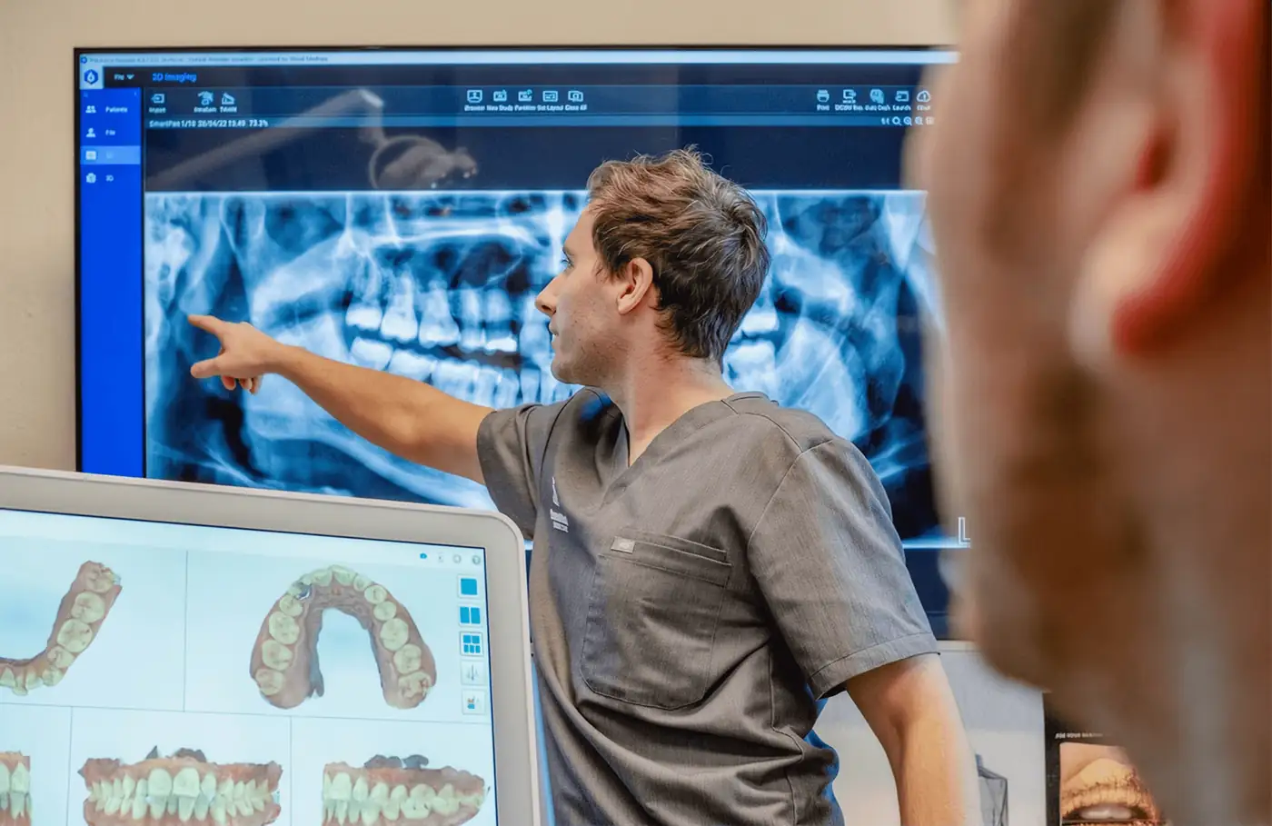 A dentist talking a patient through x-rays on a screen